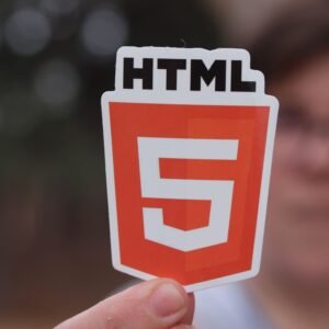A close-up of an HTML5 logo sticker held by a person with a blurred background, highlighting web development.